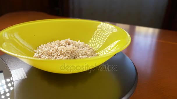 Alguien mide un pedazo de arroz integral, en una balanza electrónica en la cocina. vierta la grupa en un recipiente redondo profundo, de pie sobre una plataforma de pesaje plana. 4k, cámara lenta, dolly shot — Vídeos de Stock