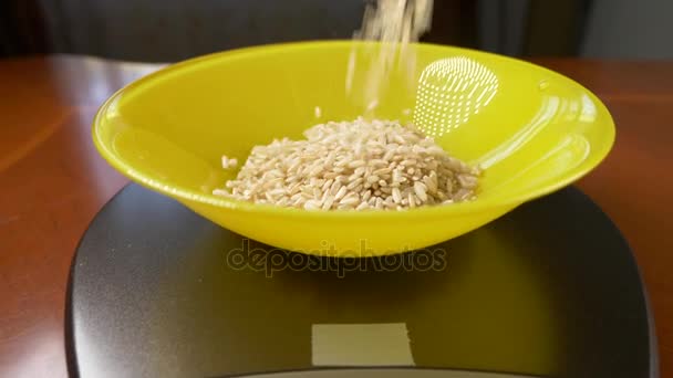 Någon mäter en bit brunt ris, på en elektronisk våg i köket. Häll en djup rund skål, stående på en platt väger plattform gumpen. 4k, ultrarapid, dolly skott — Stockvideo
