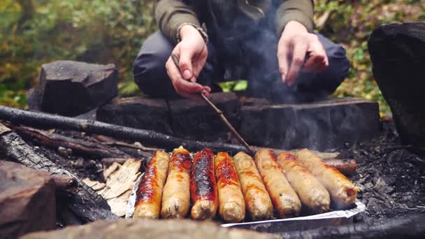 4K, câmara lenta. o turista está cozinhando salsichas em uma mini churrasqueira na floresta. close-up — Vídeo de Stock