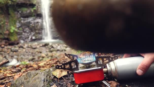 4k, slow-motion. de toerist draait op de gasbrander aan de voet van de berg, tegen de waterval. — Stockvideo