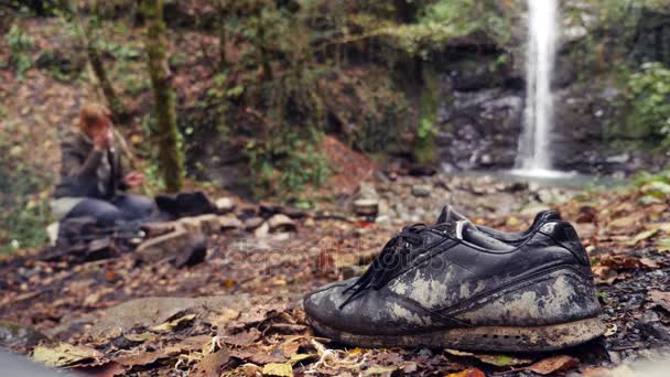 4K, câmara lenta. Sapatos turísticos sujos no fundo de uma cachoeira no sopé da montanha — Vídeo de Stock