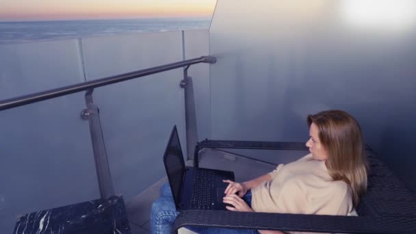 4k. жінка працює на ноутбуці на балконі курортного готелю з видом на море. Віддалена робота будь-де . — стокове відео
