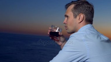 tatil balkondan Deniz Manzaralı duran bir adam. batımını akşam kokteyl içer. 4k