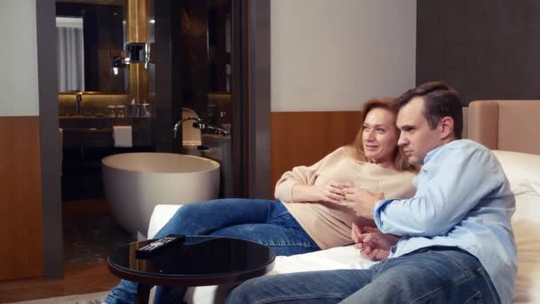 Belo casal apaixonado assistindo TV e bebendo em um hotel. 4k — Vídeo de Stock