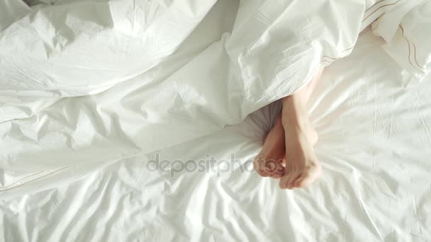 Pernas femininas na vista da cama de cima, roupa de cama branca, 4k — Vídeo de Stock