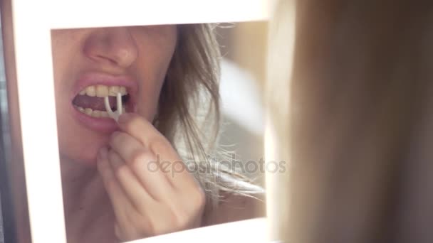 4К, крупный план. Женщина использует зубную нить в ванной комнате перед зеркалом — стоковое видео