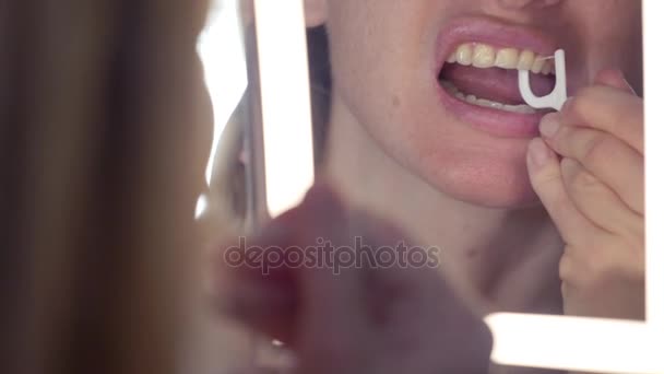 4К, крупный план. Женщина использует зубную нить в ванной комнате перед зеркалом — стоковое видео