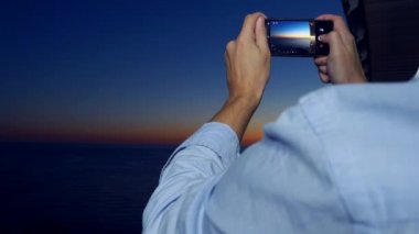 Bir spa otel balkonda bir smartphone kullanarak çekici bir genç adam, bir adam güneşin deniz kenarı kullanmayan bir uygulama kullanırken Smartphone'da çekiyor. 4 k yakın çekim