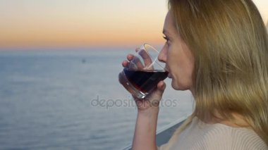 bir kadın tatil deniz manzaralı balkon üzerinde duruyor. batımını akşam kokteyl içer. 4k