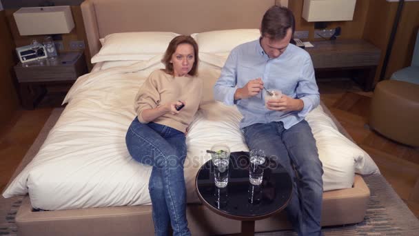Pár muž a žena, vegetariáni, sedí večer v posteli, sledování televize a jíst brokolici. 4k — Stock video