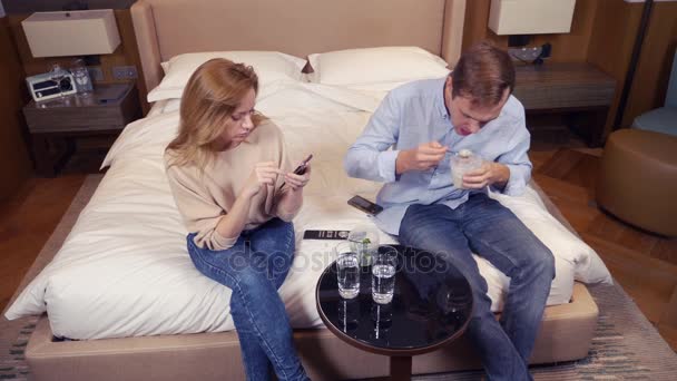 Een paar man en vrouw, vegetariërs, zitten in de avond op het bed, Tv kijken en eten van broccoli. 4k — Stockvideo