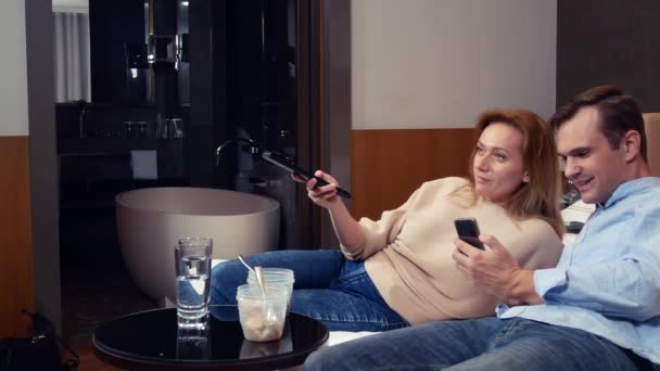 Um casal de homens e mulheres, vegetarianos, sentados à noite na cama, assistindo TV e comendo brócolis. 4k — Vídeo de Stock