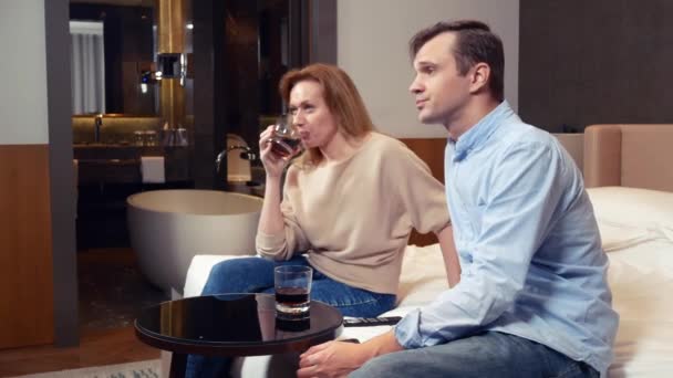 Hermosa pareja enamorada viendo televisión y bebiendo en un hotel. 4k — Vídeos de Stock