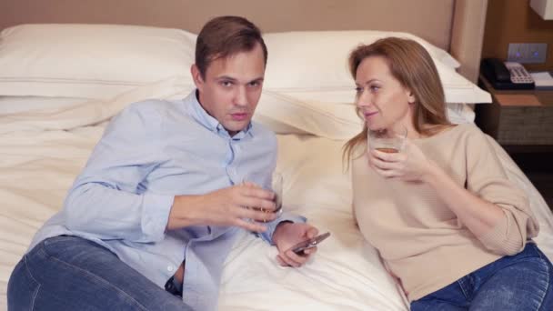 Hermosa pareja enamorada viendo televisión y bebiendo en un hotel. 4k — Vídeo de stock