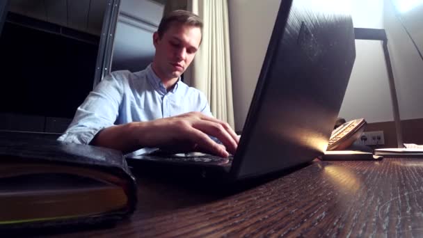 Un hombre trabajando en un portátil en una mesa por la noche en una habitación de hotel. 4k . — Vídeos de Stock