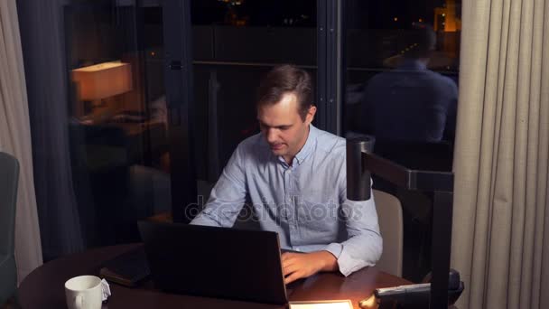 Un hombre trabajando en un portátil en una mesa por la noche en una habitación de hotel. 4k . — Vídeos de Stock