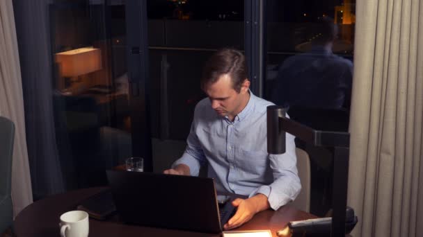 Man working on a laptop at a table at night in a hotel room. 4k. — Stock Video