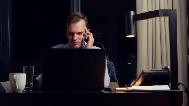 Mann arbeitet nachts an einem Laptop an einem Tisch in einem Hotelzimmer. 4k. — Stockvideo