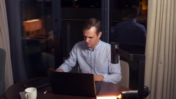 Un hombre trabajando en un portátil en una mesa por la noche en una habitación de hotel. 4k . — Vídeo de stock