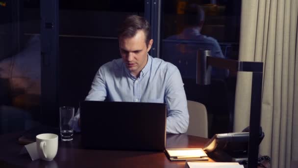 Muž pracuje na notebooku u stolu v noci v hotelovém pokoji. 4k. — Stock video