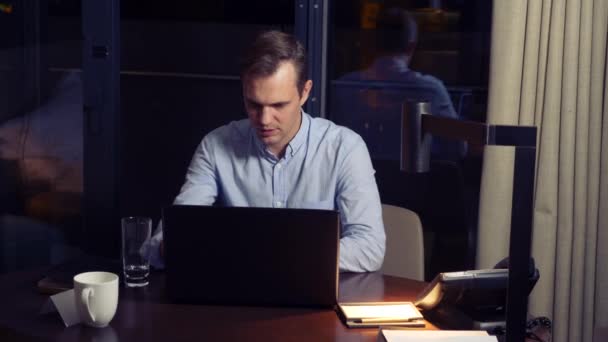 Man aan het werk op een laptop aan een tafel bij nacht in een hotelkamer. 4k. — Stockvideo