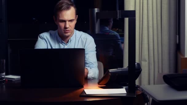 Adam bir masada bir dizüstü bilgisayarda çalışma gece bir otel odasında. 4k. — Stok video