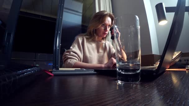 Woman working on a laptop at a table at night in a hotel room. 4k. — Stock Video