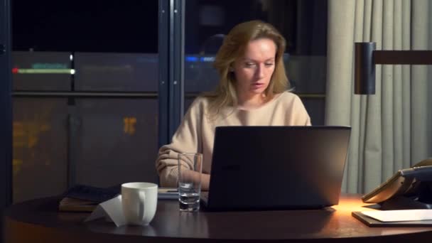 Mujer trabajando en un portátil en una mesa por la noche en una habitación de hotel. 4k . — Vídeo de stock