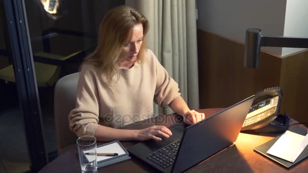 Женщина, работающая на ноутбуке за столом ночью в номере отеля. 4k . — стоковое видео