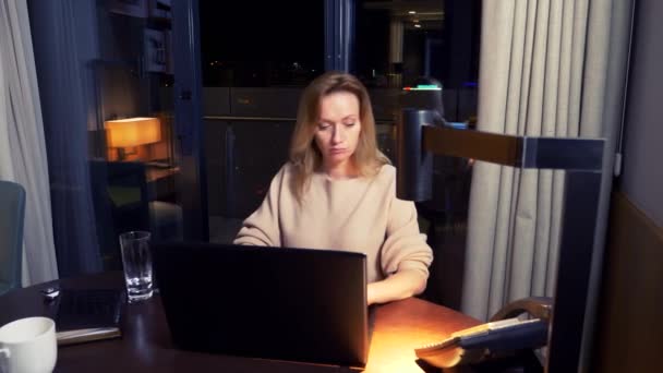 Mujer trabajando en un portátil en una mesa por la noche en una habitación de hotel. 4k . — Vídeo de stock