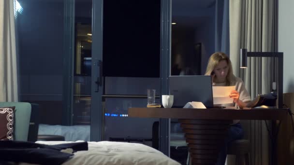 Mujer trabajando en un portátil en una mesa por la noche en una habitación de hotel. 4k . — Vídeos de Stock