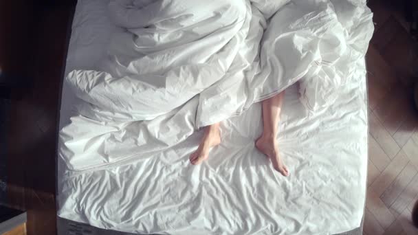 Par i sängen att älska. manliga och kvinnliga ben ovanifrån, vita sängkläder. kön, 4k — Stockvideo