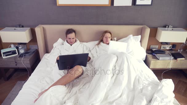 Pareja joven acostada en la cama usando computadora portátil, charlando en línea, chica y hombre en el dormitorio. Buenos días. 4k — Vídeos de Stock