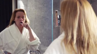 Beyaz bornoz giyen kadın ayna, 4 k önünde diş fırçaları