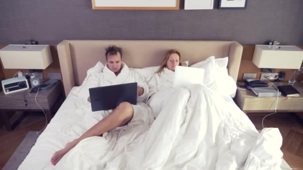 Casal jovem deitado na cama usando computador portátil, conversando on-line, menina e homem no quarto. Bom dia. 4k — Vídeo de Stock