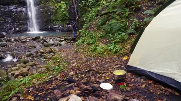 4k, slow-motion. toeristische bowler op een brander aan de voet van de berg, tegen een waterval — Stockvideo