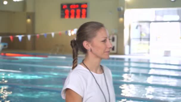 女孩游泳教练, 跟随游泳者的锻炼, 转过来, 看入照相机和微笑, 4k, 慢动作 — 图库视频影像