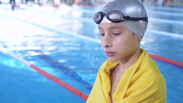 Портрет хлопчика-спортсмена в окулярах для плавання та шапка для плавання з рушником після тренування, на тлі спортивного басейну. 4k, повільний рух, крупним планом — стокове відео