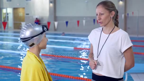 Simma atlet utbildning. Tränaren pratar med pojken efter utbildning på bakgrund av en sport-pool. 4k, Slowmotion — Stockvideo