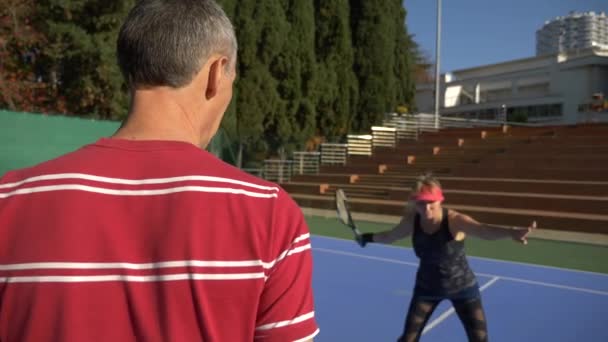 Игроки разогреваются перед игрой в теннис. Старший мужчина и женщина играют в теннис. 4k — стоковое видео