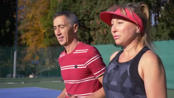 Los jugadores se calientan antes de un partido de tenis. Hombre y mujer mayores jugando tenis. 4k — Vídeos de Stock
