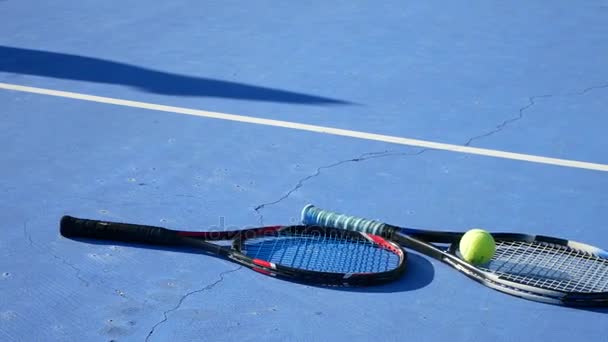 Una pelota de tenis y raquetas de tenis se encuentran en la cancha en un día claro y soleado. 4k . — Vídeos de Stock