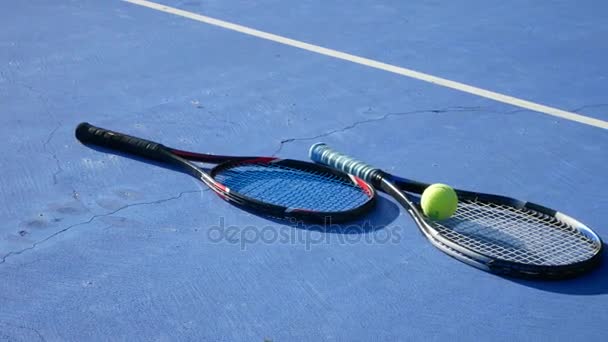 Una pelota de tenis y raquetas de tenis se encuentran en la cancha en un día claro y soleado. 4k . — Vídeo de stock