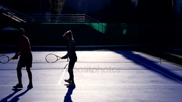 Hráči se zahřát před zahrát tenis. Starší muž a žena hrát tenis. 4k, siluety — Stock video