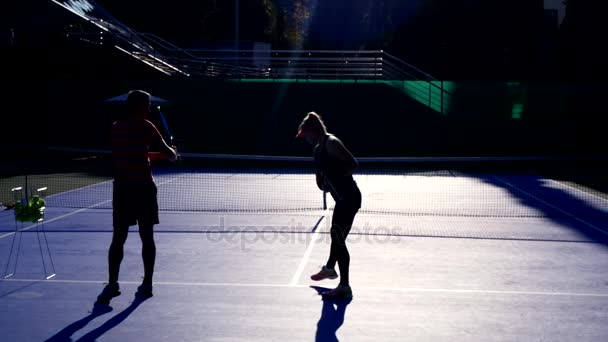 Игроки разогреваются перед игрой в теннис. Старший мужчина и женщина играют в теннис. 4к, силуэты — стоковое видео