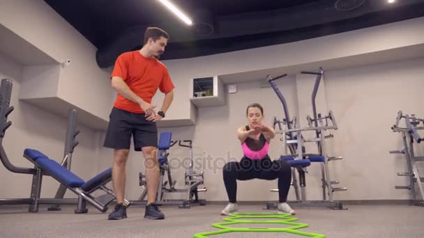 Молодая взрослая девушка занимается на тренажерах под руководством своего личного тренера. 4k, slow motion — стоковое видео