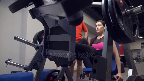 Menina adulta jovem fazendo um treino sobre os simuladores liderados por seu personal trainer. 4k, câmera lenta — Vídeo de Stock