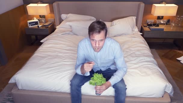 Hombre hombre de negocios come vegetariano comer hojas de col en un vaso. sentado frente al televisor. 4k — Vídeo de stock