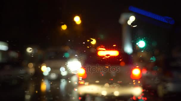 La lluvia fluye y limpiaparabrisas en la ventana de cristal del parabrisas delantero del coche que se detiene al lado de la carretera con la luz borrosa colorida hermosa del tráfico afuera en la carretera. 4k — Vídeo de stock