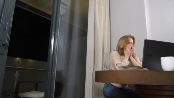 Mujer trabajando en un portátil en una mesa por la noche en una habitación de hotel. 4k. se duerme en el lugar de trabajo, bosteza . — Vídeo de stock
